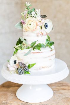 a three tiered cake with flowers and leaves on top is sitting on a table