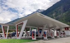 a gas station with mountains in the background and cars parked at it's charging stations