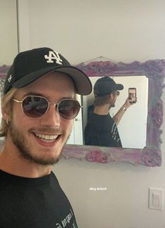 a man taking a selfie in front of a mirror wearing sunglasses and a baseball cap