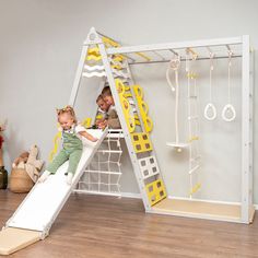 two children are playing on a white and yellow play set with ladders, climbing ropes, and toys