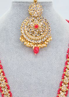 Get ready to make a statement with this stunning Kundan necklace set. Its bold circular design and lively pearl embellishments are accentuated by a daring Kundan feature. Perfect for any celebratory occasion! Necklace Length: 16" Neckline has an adjustable doori. Earring Lenght: 3" Push-Back closure Weight : 40 gms Maang Tiika Length: 3" Weight : 23 gms Gold finish on high-quality brass as a base metal. Availability: In-Stock. *Color may vary slightly due to light condition & photography. Jewelr Round Necklaces For Festive Party, Festive Party Necklaces, Festive Round Beaded Kundan Necklace, Adjustable Round Jewelry Sets For Festive Occasions, Adjustable Festive Jewelry Sets, Kundan Round Necklace For Parties, Round Pearl Necklace For Festivals, Round Pearl Necklace For Celebrations And Festivals, Red Jewelry For Festival Party