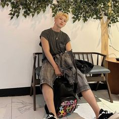 a young man sitting on top of a piece of luggage next to a tree in a room