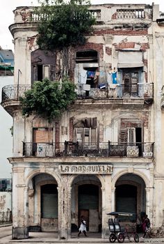 an old building with balconies on the top floor and two people walking by