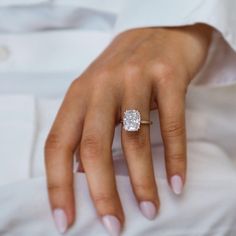 a woman's hand with a diamond ring on her left hand, wearing a white shirt