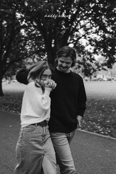 black and white photograph of two people walking together in the park with trees behind them