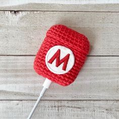 a red knitted object with the letter m on it is plugged into an ipod charger