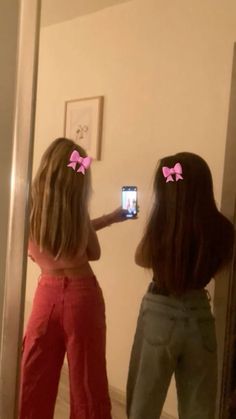 two girls with pink bows on their hair are looking at themselves in the bathroom mirror