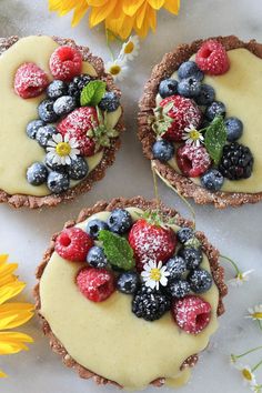 three desserts with fruit on top of them and flowers in the backgroud