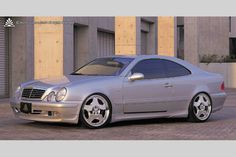 a silver mercedes benz coupe parked in front of a building on a brick road with doors open