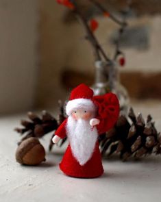 a small red and white santa clause doll next to pine cones