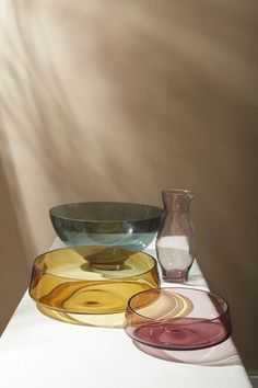 three different colored glass bowls sitting on top of a white tablecloth next to a vase