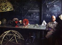 a man sitting in front of a blackboard filled with different shapes and sizes on it