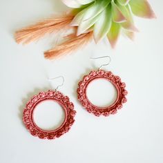 two pairs of pink earrings sitting on top of a white table next to a flower