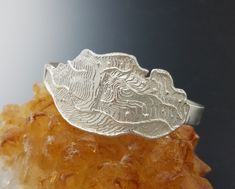 This is a beautiful casting and one of my all time favorites.  Winding Roads and Mountains were my inspiration for this unique cuff bracelet. It was made from sterling silver cast in cuttlefish bone.  I first carved the design in the bone and created a mold.  Then I poured molten metal into the bone mold.  The silver came out of the mold like this.  I loved the organic shapes of the edges and so I left them in their natural state. This bracelet was created as a one of a kind work of art. At its Unique Bangle Bracelets For Anniversary, Unique Sterling Silver Cuff Bracelet For Wedding, Unique Oyster Bracelet Jewelry For Anniversary, Unique Hand Cast Bracelets As Gift, Unique Sterling Silver Bangle For Anniversary, Unique Engraved Anniversary Bracelets, Unique Bangle Jewelry For Anniversary, Unique Bangle For Anniversary, Hand Cast Silver Bangle As A Gift