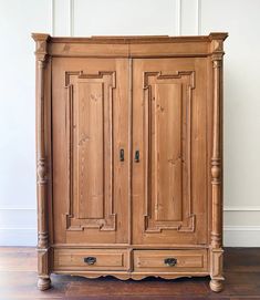 an old wooden armoire sitting on top of a hard wood floor next to a white wall