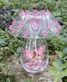 a glass lamp with pink butterflies on it in front of some bushes and plants,