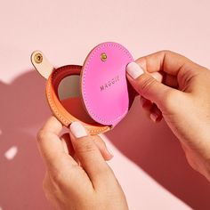 a person holding a pink compact case in their hand, with the lid open to show it's inside