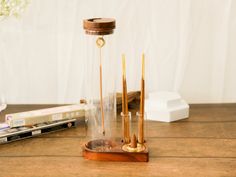 a wooden table topped with a glass vase filled with water and gold colored metal tubes