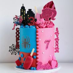 a birthday cake decorated with pink and blue frosting, spiderman decorations and candy