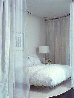 a white bed sitting on top of a wooden floor next to a curtained window