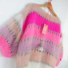 a pink and white sweater hanging on a hanger with a tag attached to it