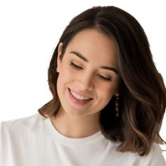 a woman smiles as she looks down at her cell phone while wearing a white t - shirt