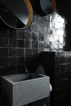 a sink and mirror in a black tiled bathroom with two circular mirrors on the wall