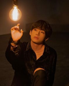 a young man sitting on the ground holding up a light bulb