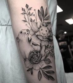 a woman's arm with flowers on it and two rabbits in the center, surrounded by leaves