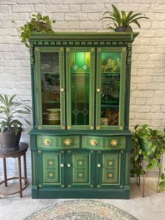 a green china cabinet sitting next to a potted plant on top of a rug