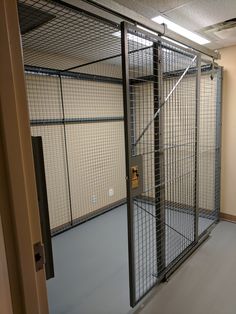 an empty room with a metal cage on the wall and door to another room behind it