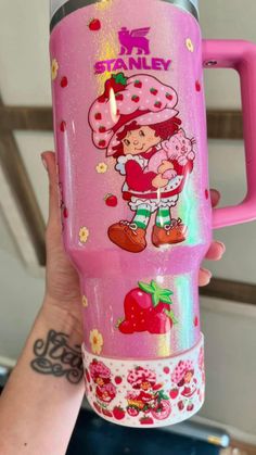 a person holding up a pink cup with strawberries and strawberrys painted on it