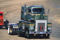 a large green semi truck driving down a dirt road next to a man on a motorcycle