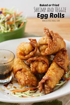 fried shrimp and veggie egg rolls on a white plate next to a bowl of coleslaw