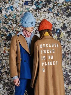 two people standing next to each other in front of a wall covered with plastic trash