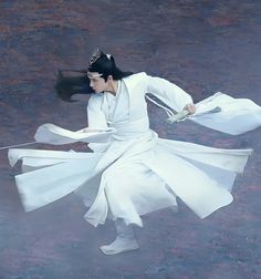 a woman dressed in white is performing on the ground with her long hair flying through the air