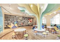 children are sitting at tables and chairs in the library with colorful trees painted on the walls