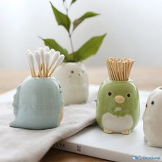 three ceramic animals with toothpicks in their mouths on a white towel next to a potted plant