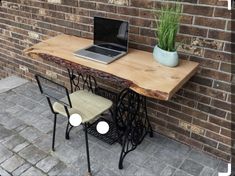 a laptop computer sitting on top of a wooden table next to a chair and brick wall