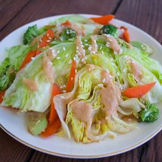 a white plate topped with lettuce and carrots covered in sesame seed dressing