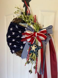 a patriotic wreath with red, white and blue ribbons hanging from the front door on a door hanger