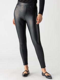 A person is shown from the shoulders down, wearing Sanctuary Clothing's Runway Legging Slick Black and a black long-sleeved top. They are also wearing black flat shoes and a simple gold ring. The background is plain white. Stretch Solid Color Polyurethane Leather Pants, Sleek Solid Color Faux Leather Leggings, Sleek High Stretch Black Leather Pants, Sleek Stretch Faux Leather Leggings, Sleek Tight Faux Leather Leggings, Sleek Solid Faux Leather Pants, Black High Stretch Full Length Leather Pants, Stretch Full-length Black Leather Pants, Sleek High Stretch Faux Leather Leggings