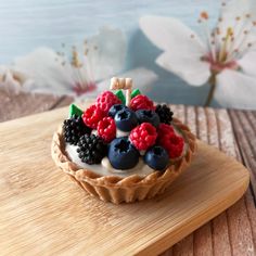 a fruit tart with berries and blueberries on top sits on a wooden board