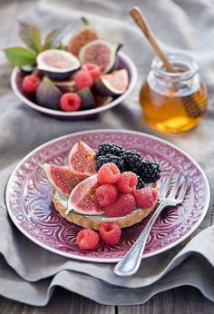 a pink plate topped with fruit next to a jar of honey