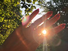 someone's hand with red nail polish holding up the sun