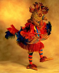 an elaborately decorated bird is standing in front of a yellow background with red, blue and orange feathers