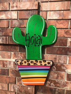 a green cactus with the word hola painted on it's side next to a brick wall