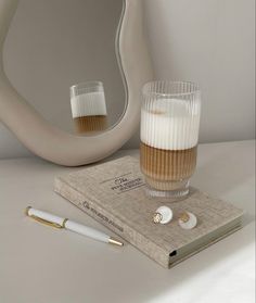 a book, pen and glass on a table with a mirror in the back ground