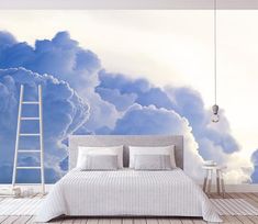 a bed sitting under a blue sky filled with clouds next to a white chair and table