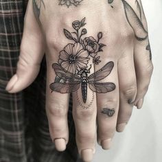 a woman's hand with a dragonfly and flowers tattoo on the ring finger